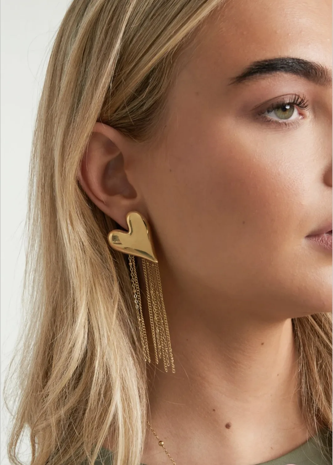 By Jeanny Heart Earrings – Christmas Edition; goudkleurige stainless-steel oorbellen met glanzend hart en fijne kettingdetails, feestelijke damesoorbellen voor de kerstcollectie.